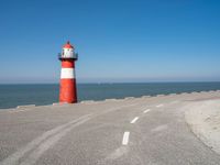 the road has a light house with a red top on the top of it next to the ocean