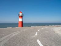 the road has a light house with a red top on the top of it next to the ocean