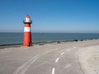 the road has a light house with a red top on the top of it next to the ocean