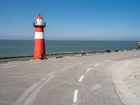 the road has a light house with a red top on the top of it next to the ocean