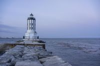 there is a lighthouse on the side of the rock wall by the water, and the light house is also near a dock