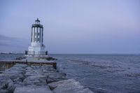 there is a lighthouse on the side of the rock wall by the water, and the light house is also near a dock