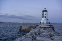 there is a lighthouse on the side of the rock wall by the water, and the light house is also near a dock