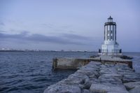 there is a lighthouse on the side of the rock wall by the water, and the light house is also near a dock