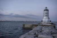 there is a lighthouse on the side of the rock wall by the water, and the light house is also near a dock