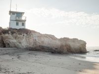 a lighthouse stands high on a rocky cliff at the beach with footprints in the sand