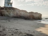 a lighthouse stands high on a rocky cliff at the beach with footprints in the sand