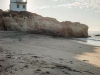 a lighthouse stands high on a rocky cliff at the beach with footprints in the sand