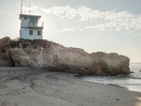 a lighthouse stands high on a rocky cliff at the beach with footprints in the sand