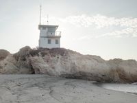 a lighthouse stands high on a rocky cliff at the beach with footprints in the sand