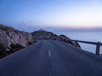 a lighthouse sitting above the ocean and a road leading to it on a hill at sunset