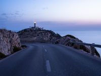 a lighthouse sitting above the ocean and a road leading to it on a hill at sunset