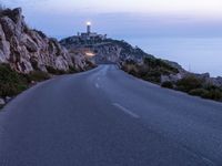 a lighthouse sitting above the ocean and a road leading to it on a hill at sunset