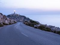 a lighthouse sitting above the ocean and a road leading to it on a hill at sunset