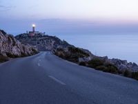 a lighthouse sitting above the ocean and a road leading to it on a hill at sunset