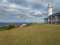 the lighthouse tower is surrounded by a long grassy hill overlooking the ocean and the ocean