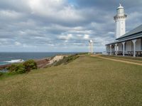 the lighthouse tower is surrounded by a long grassy hill overlooking the ocean and the ocean