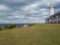 the lighthouse tower is surrounded by a long grassy hill overlooking the ocean and the ocean