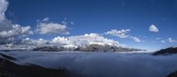 clouds roll in the valley below a mountain range as seen from a viewpoint point on the mountain