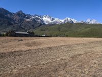 a field with a couple of horses in it with mountains in the background near some snow capped peaks