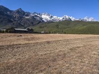 a field with a couple of horses in it with mountains in the background near some snow capped peaks