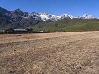 a field with a couple of horses in it with mountains in the background near some snow capped peaks