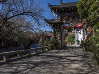 lanterns stand on the end of an archway leading to some chinese buildings in a park