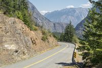 the mountains surrounding a road that is steep and full of dirt and pine trees along its sides