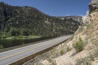 the paved road next to the river flows into a scenic area with many cliffs near a lake