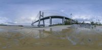 a reflection of a large bridge across a body of water below it is a cloudy sky