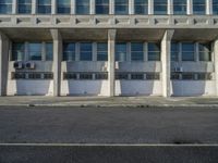 an old white concrete building has many doors in front of it and the sidewalk is in front of it