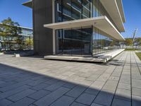 a walkway leads to the front facade of a glass and concrete building with benches and trees on either side