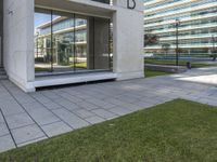 an empty walkway leads to the entrance of a building on which the exterior is glass