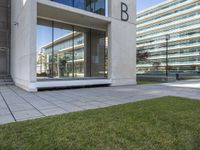 an empty walkway leads to the entrance of a building on which the exterior is glass