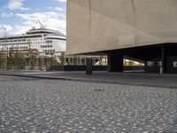 a tall white building with a giant black ship in the background and some people walking around