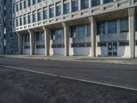 an empty street in front of some concrete and brick buildings with tall windows and long columns