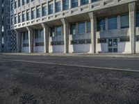 an empty street in front of some concrete and brick buildings with tall windows and long columns