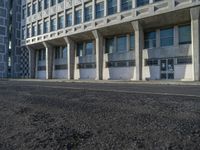 an empty street in front of some concrete and brick buildings with tall windows and long columns