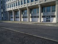 an empty street in front of some concrete and brick buildings with tall windows and long columns