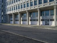 an empty street in front of some concrete and brick buildings with tall windows and long columns