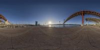 a panoramic shot of a bridge near the water with a sunset behind it