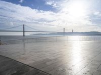 a walkway with no people near the ocean next to a bridge and a boat on the water