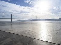 a walkway with no people near the ocean next to a bridge and a boat on the water