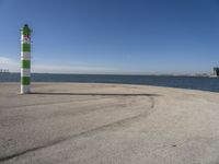 a blue sky, light house and a green and white pillar near the water's edge