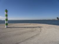 a blue sky, light house and a green and white pillar near the water's edge