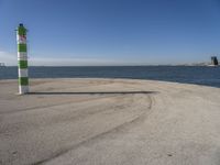 a blue sky, light house and a green and white pillar near the water's edge