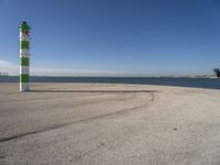 a blue sky, light house and a green and white pillar near the water's edge