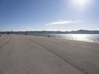 a person is skateboarding down a stretch of beach near a body of water with mountains in the distance