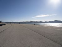 a person is skateboarding down a stretch of beach near a body of water with mountains in the distance