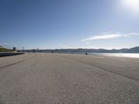 a person is skateboarding down a stretch of beach near a body of water with mountains in the distance